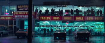 Movie still from “White Noise” (2022), directed by Noah Baumbach – A car parked in front of a store with people standing outside; Extreme Wide shot, High angle