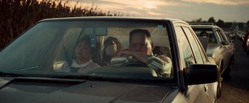 Movie still from “White Noise” (2022), directed by Noah Baumbach – A man and a woman in a car with another man in the back seat; Medium shot, Low angle