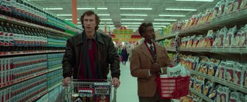 Movie still from “White Noise” (2022), directed by Noah Baumbach – Two men are walking through a grocery store with shopping carts; Medium shot, Over the shoulder angle