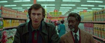Movie still from “White Noise” (2022), directed by Noah Baumbach – Two men standing in a grocery store , one of whom is wearing a jacket; Medium shot, Low angle