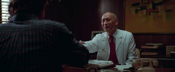 Movie still from “White Noise” (2022), directed by Noah Baumbach – A man in a white lab coat shaking hands with another man; Medium shot, Over the shoulder angle