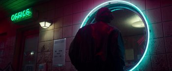 Movie still from “White Noise” (2022), directed by Noah Baumbach – A man standing in front of a round neon sign; Medium shot, Low angle