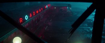 Movie still from “White Noise” (2022), directed by Noah Baumbach – A view of a night scene with a neon sign lit up; Extreme Wide shot, High angle
