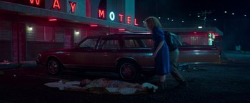Movie still from “White Noise” (2022), directed by Noah Baumbach – A woman walking past a man laying on the ground in front of a motel; Wide shot, Low angle