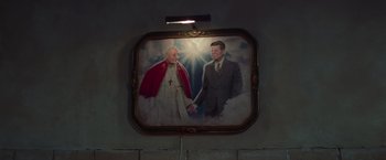 Movie still from “White Noise” (2022), directed by Noah Baumbach – A painting of two men holding hands in front of a wall; Medium shot, Low angle