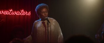 Movie still from “Whitney Houston: I Wanna Dance with Somebody” (2022), directed by Kasi Lemmons – A woman is singing into a microphone in front of a crowd; Medium shot, Over the shoulder angle