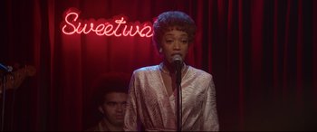 Movie still from “Whitney Houston: I Wanna Dance with Somebody” (2022), directed by Kasi Lemmons – A woman standing in front of a microphone on a stage; Medium shot, Over the shoulder angle