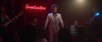 Movie still from “Whitney Houston: I Wanna Dance with Somebody” (2022), directed by Kasi Lemmons – A woman standing in front of a microphone on a stage; Medium shot, Over the shoulder angle