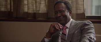 Movie still from “Whitney Houston: I Wanna Dance with Somebody” (2022), directed by Kasi Lemmons – A man in a suit and tie smiling for the camera; Close Up shot, Over the shoulder angle