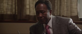 Movie still from “Whitney Houston: I Wanna Dance with Somebody” (2022), directed by Kasi Lemmons – An older man in a suit and tie looking to his left; Close Up shot, Over the shoulder angle