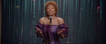 Movie still from “Whitney Houston: I Wanna Dance with Somebody” (2022), directed by Kasi Lemmons – A woman in a purple dress singing into a microphone; Medium shot, Low angle