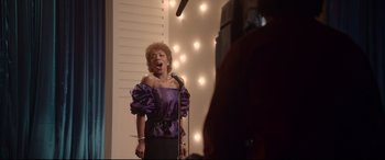 Movie still from “Whitney Houston: I Wanna Dance with Somebody” (2022), directed by Kasi Lemmons – A woman in a purple dress singing into a microphone; Medium shot, Low angle