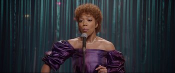 Movie still from “Whitney Houston: I Wanna Dance with Somebody” (2022), directed by Kasi Lemmons – A woman in a purple dress is holding a microphone; Medium shot, Over the shoulder angle