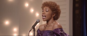 Movie still from “Whitney Houston: I Wanna Dance with Somebody” (2022), directed by Kasi Lemmons – A woman in a purple dress singing into a microphone; Close Up shot, Low angle