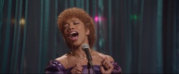 Movie still from “Whitney Houston: I Wanna Dance with Somebody” (2022), directed by Kasi Lemmons – A woman in a purple dress singing into a microphone; Close Up shot, Low angle