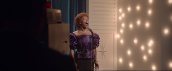 Movie still from “Whitney Houston: I Wanna Dance with Somebody” (2022), directed by Kasi Lemmons – A woman in a purple dress singing into a microphone; Medium shot, Low angle