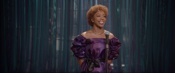Movie still from “Whitney Houston: I Wanna Dance with Somebody” (2022), directed by Kasi Lemmons – A woman in a purple dress holding a microphone; Medium shot, Over the shoulder angle
