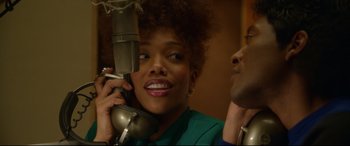 Movie still from “Whitney Houston: I Wanna Dance with Somebody” (2022), directed by Kasi Lemmons – A woman holding a microphone up to her ear while a man looks on; Close Up shot, Over the shoulder angle