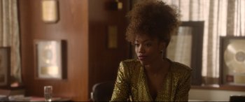 Movie still from “Whitney Houston: I Wanna Dance with Somebody” (2022), directed by Kasi Lemmons – A woman in a gold jacket sitting at a table; Close Up shot, Over the shoulder angle