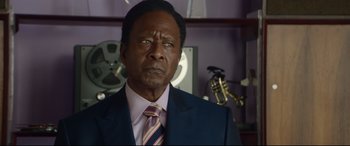 Movie still from “Whitney Houston: I Wanna Dance with Somebody” (2022), directed by Kasi Lemmons – A man in a suit and tie in front of a clock; Close Up shot, Over the shoulder angle