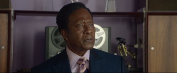 Movie still from “Whitney Houston: I Wanna Dance with Somebody” (2022), directed by Kasi Lemmons – A man in a suit and tie in front of an old movie projector; Close Up shot, Over the shoulder angle