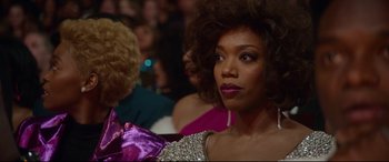 Movie still from “Whitney Houston: I Wanna Dance with Somebody” (2022), directed by Kasi Lemmons – A woman sitting in a crowd of people; Close Up shot, Over the shoulder angle