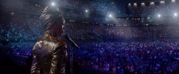 Movie still from “Whitney Houston: I Wanna Dance with Somebody” (2022), directed by Kasi Lemmons – A woman is speaking on a microphone in front of an audience; Extreme Wide shot, High angle
