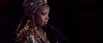 Movie still from “Whitney Houston: I Wanna Dance with Somebody” (2022), directed by Kasi Lemmons – A woman in a gold dress is holding a microphone; Close Up shot, Over the shoulder angle