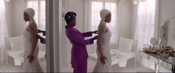 Movie still from “Whitney Houston: I Wanna Dance with Somebody” (2022), directed by Kasi Lemmons – A woman in a purple suit is helping another woman in a white dress; Medium shot, Over the shoulder angle