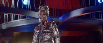 Movie still from “Whitney Houston: I Wanna Dance with Somebody” (2022), directed by Kasi Lemmons – A woman is singing into a microphone on a stage; Medium shot, Over the shoulder angle