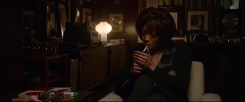 Movie still from “Whitney Houston: I Wanna Dance with Somebody” (2022), directed by Kasi Lemmons – A woman sitting in a chair holding a cigarette in her hand; Medium shot, High angle