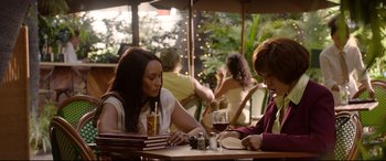 Movie still from “Whitney Houston: I Wanna Dance with Somebody” (2022), directed by Kasi Lemmons – Two women sitting at an outdoor table with a glass of red wine; Medium shot, Over the shoulder angle
