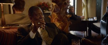 Movie still from “Whitney Houston: I Wanna Dance with Somebody” (2022), directed by Kasi Lemmons – A man sitting on a couch in a living room; Close Up shot, Over the shoulder angle