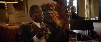 Movie still from “Whitney Houston: I Wanna Dance with Somebody” (2022), directed by Kasi Lemmons – A man in a suit and tie sitting in front of a table; Close Up shot, Low angle