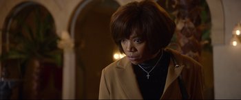 Movie still from “Whitney Houston: I Wanna Dance with Somebody” (2022), directed by Kasi Lemmons – A woman in a brown jacket with a cross on her neck; Close Up shot, Over the shoulder angle