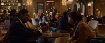 Movie still from “Whitney Houston: I Wanna Dance with Somebody” (2022), directed by Kasi Lemmons – A group of people sitting at a table in a room; Medium shot, Over the shoulder angle
