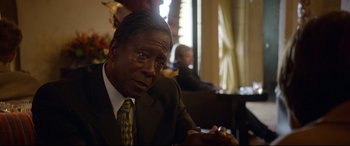 Movie still from “Whitney Houston: I Wanna Dance with Somebody” (2022), directed by Kasi Lemmons – A man in a suit and tie looking at a cell phone; Close Up shot, Over the shoulder angle