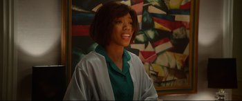Movie still from “Whitney Houston: I Wanna Dance with Somebody” (2022), directed by Kasi Lemmons – A woman smiling in front of an abstract painting; Medium shot, Over the shoulder angle