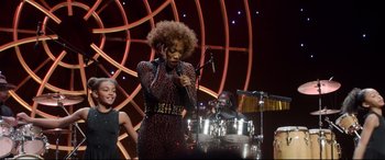 Movie still from “Whitney Houston: I Wanna Dance with Somebody” (2022), directed by Kasi Lemmons – A woman in a leopard print dress singing into a microphone; Medium shot, Over the shoulder angle