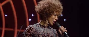Movie still from “Whitney Houston: I Wanna Dance with Somebody” (2022), directed by Kasi Lemmons – A person holding a microphone on a stage; Close Up shot, Over the shoulder angle