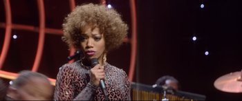 Movie still from “Whitney Houston: I Wanna Dance with Somebody” (2022), directed by Kasi Lemmons – A woman holding a microphone in front of a microphone stand; Close Up shot, Over the shoulder angle