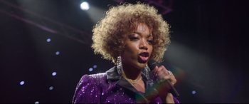 Movie still from “Whitney Houston: I Wanna Dance with Somebody” (2022), directed by Kasi Lemmons – A woman in a purple jacket holding a microphone and singing; Close Up shot, Low angle
