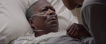 Movie still from “Whitney Houston: I Wanna Dance with Somebody” (2022), directed by Kasi Lemmons – An older man laying in a hospital bed; Close Up shot, High angle