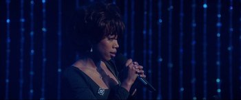 Movie still from “Whitney Houston: I Wanna Dance with Somebody” (2022), directed by Kasi Lemmons – A woman is holding a microphone and singing; Close Up shot, Over the shoulder angle