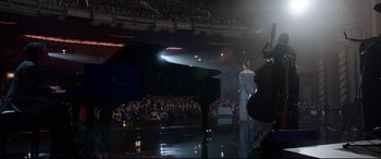 Movie still from “Whitney Houston: I Wanna Dance with Somebody” (2022), directed by Kasi Lemmons – A man standing in front of a piano on a stage; Extreme Wide shot, High angle