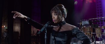 Movie still from “Whitney Houston: I Wanna Dance with Somebody” (2022), directed by Kasi Lemmons – A woman in a black dress is holding a microphone; Medium shot, Low angle
