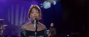 Movie still from “Whitney Houston: I Wanna Dance with Somebody” (2022), directed by Kasi Lemmons – A woman is singing into a microphone in front of a man; Close Up shot, Over the shoulder angle