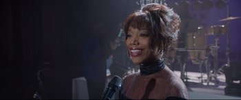 Movie still from “Whitney Houston: I Wanna Dance with Somebody” (2022), directed by Kasi Lemmons – A woman smiles while holding a microphone in her hand; Close Up shot, Over the shoulder angle