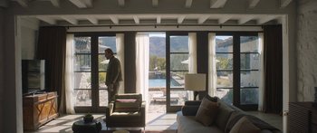 Movie still from “Windfall” (2022), directed by Charlie McDowell – A man standing in front of a living room window; Wide shot, Low angle