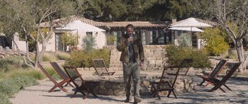 Movie still from “Windfall” (2022), directed by Charlie McDowell – A man standing in front of a stone wall; Wide shot, Over the shoulder angle